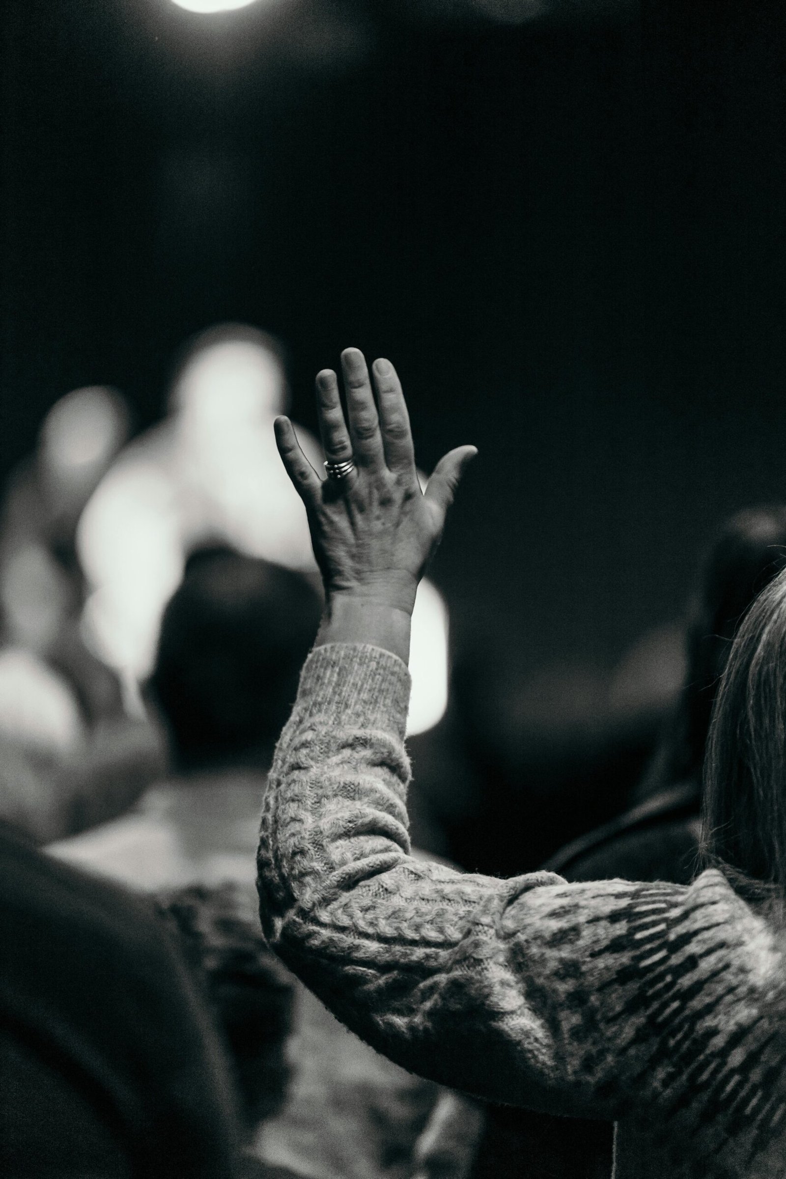 Black and white photo of a woman raising her hand in an audience, capturing engagement and curiosity.